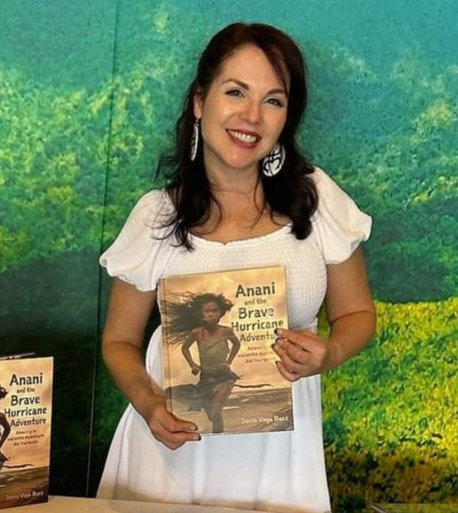Author Doris Vega Baez holding a copy of her children's book "Anani and the Brave Hurricane Adventure (Anani y la valiente aventura del huracán)"
