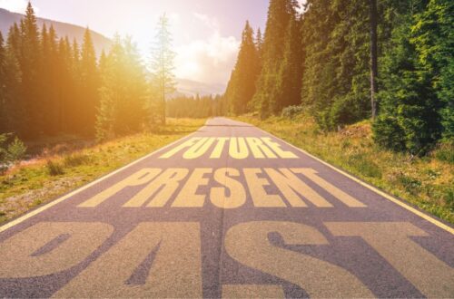 road with future, past, present written on it, road is surrounded by grass and trees and sunset in the background; past tense or present tense