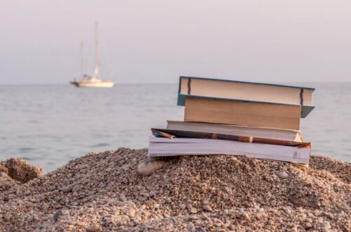 stack of books on the beach at sunset; summer reading